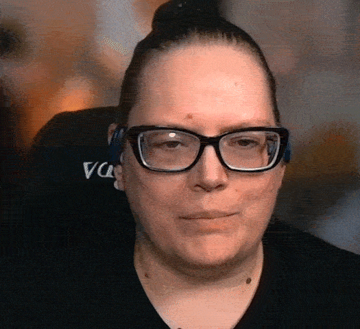 A woman with glasses and hair in a bun talking..