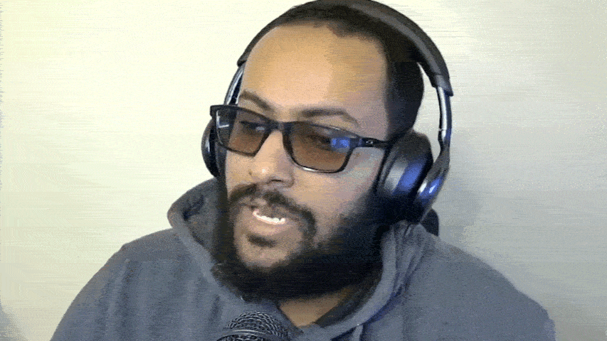 A man with a beard wearing glasses and headphones speaks into a microphone during a livestream.
