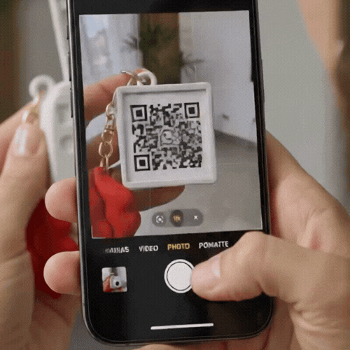 A person using a smartphone camera to scan a square QR code keychain for quick digital access.