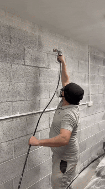 Interior cinderblock wall in the process of sprayed with grey paint, as a GIF.