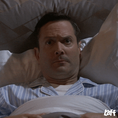 A man in striped pajamas lying in bed with a wide-eyed, shocked expression of sudden realization.