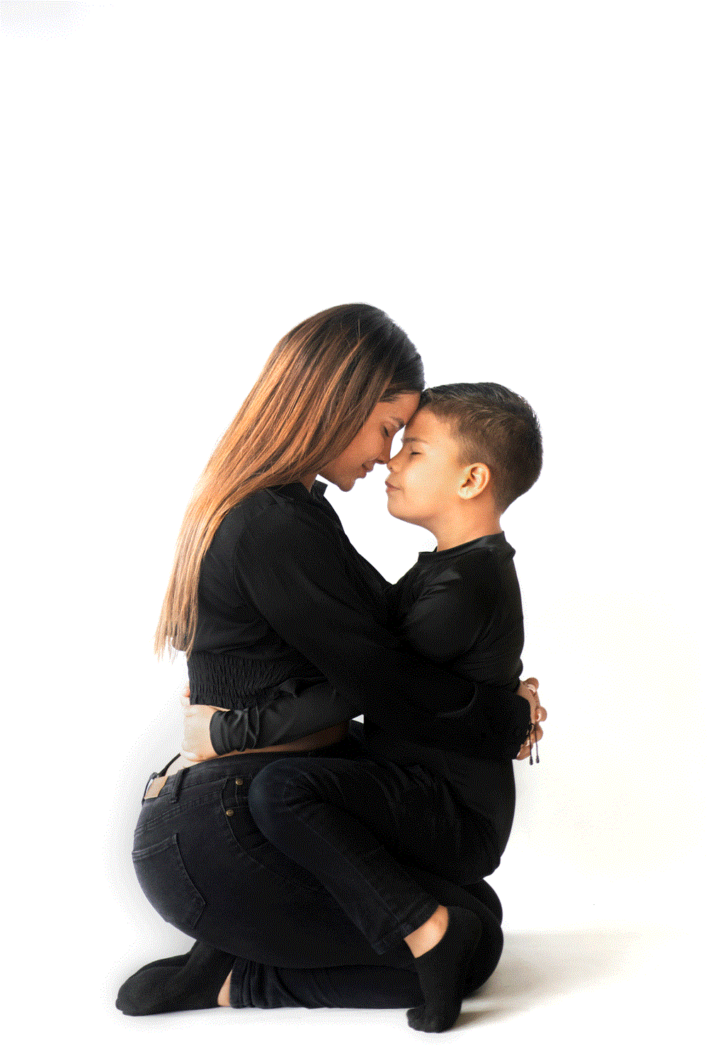 Madre e hijo abrazados, con ojos cerrados y frente con frente, en un emotivo abrazo de rodillas sobre fondo blanco.