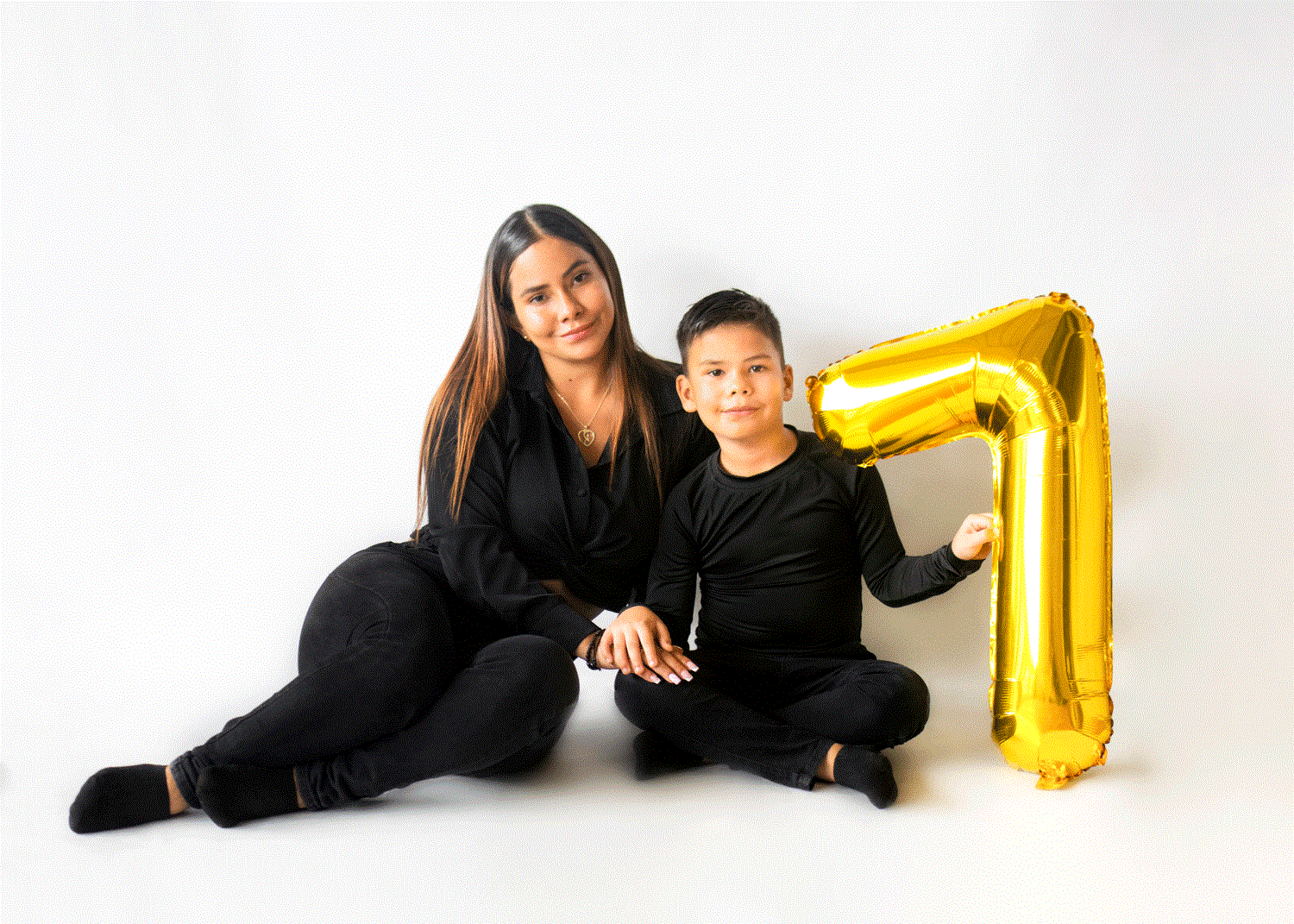 Madre e hijo sonrientes, con un globo de número 7, celebrando el cumpleaños del niño sobre fondo blanco.