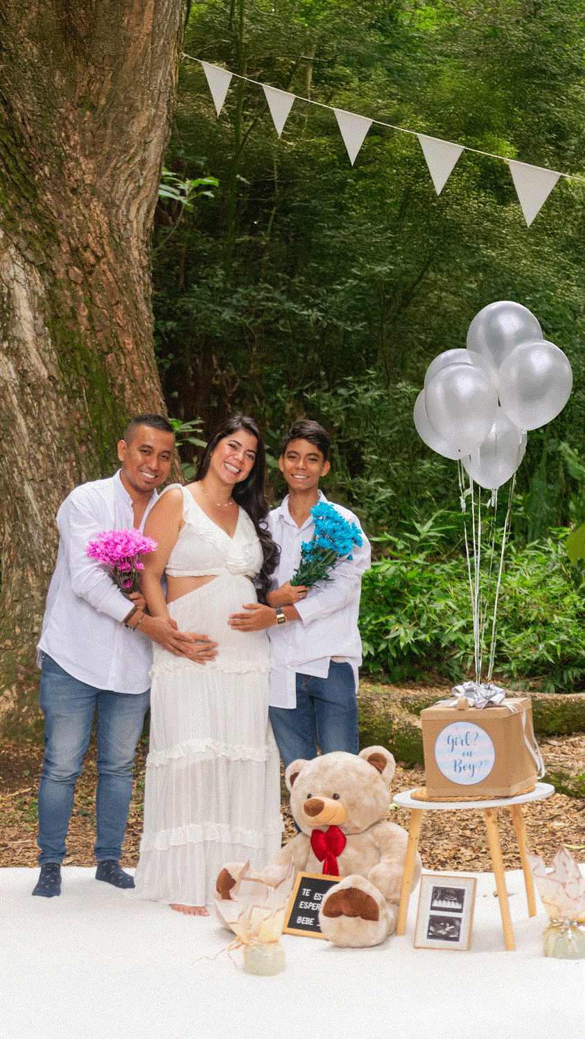 Foto familiar de revelación de género con globos, peluche y la familia (papá, mamá, hijo mayor) celebrando el embarazo.