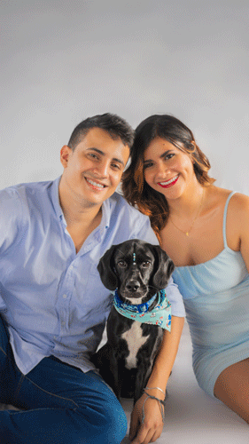 Pareja sonriente sentada con su perrito, mirando a la cámara, mostrando una conexión amorosa y familiar.