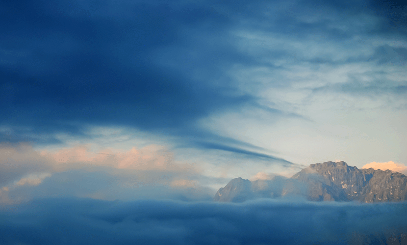 Vista panorámica de montañas a lo lejos, enmarcadas por grandes nubes, creando una atmósfera serena y majestuosa.