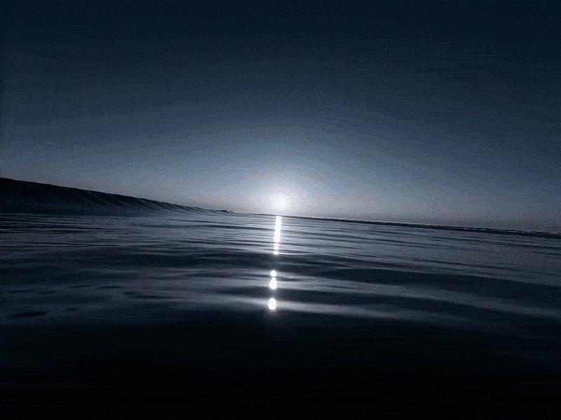 Calm ocean waves reflecting a bright sun on the horizon during a peaceful blue sunset.