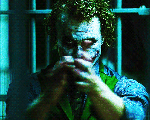 Heath Ledger's Joker character clapping and smiling behind bars in a dark Gotham jail cell.