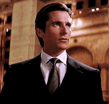 Christian Bale as Bruce Wayne in a suit, nodding slightly in a formal setting.