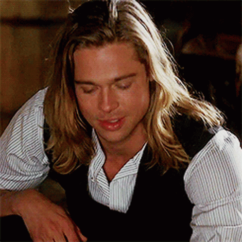 Brad Pitt as Tristan Ludlow in Legends of the Fall with long hair and a striped shirt.