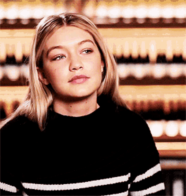 Fashion model Gigi Hadid wearing a striped black sweater during an interview with a blurred background.