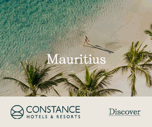 Aerial view of a person walking on a pristine white sand beach in Mauritius, bordered by turquoise ocean and palm trees