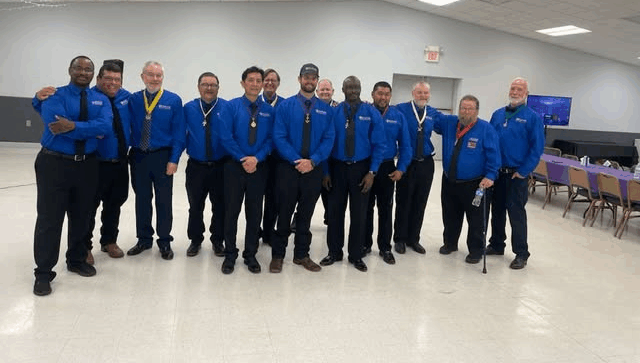 A group of Knights of Columbus men wearing blue shirts and medals pose in a banquet hall.