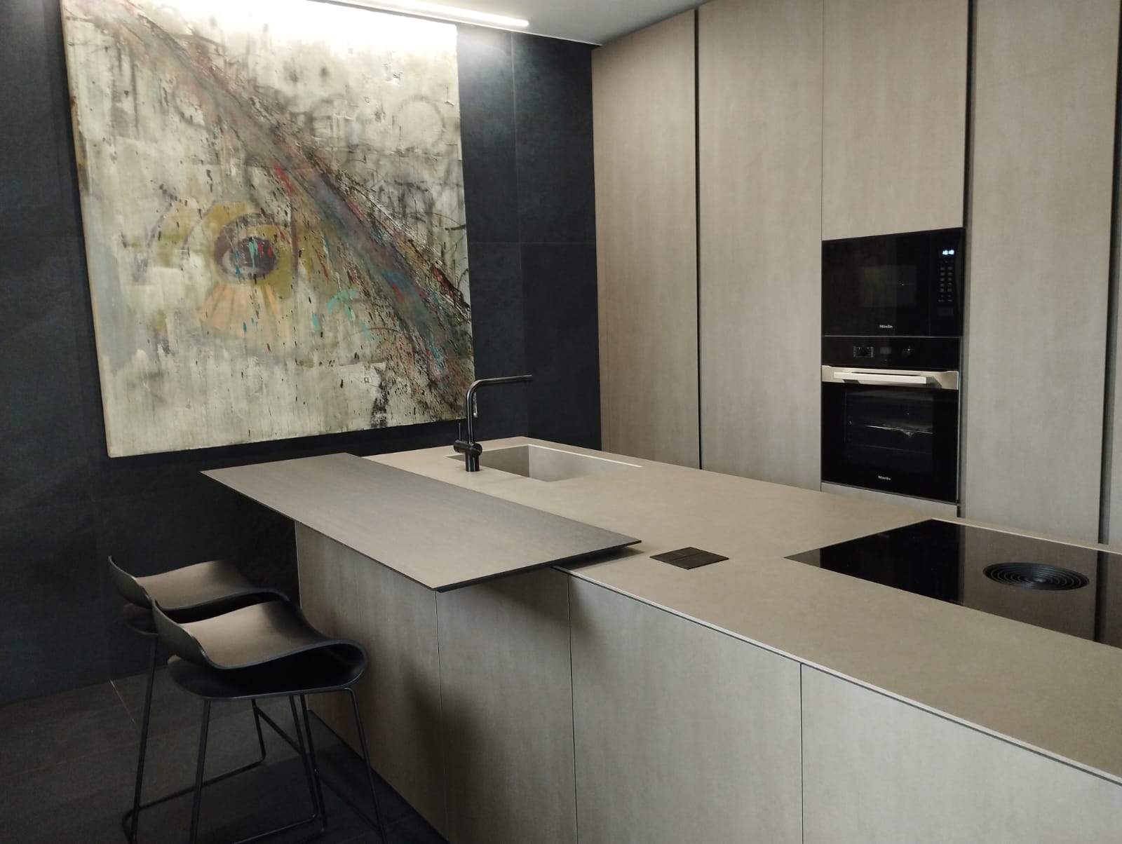 Modern minimalist kitchen featuring a concrete island, black bar stools, and abstract wall art.