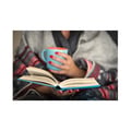 A woman wrapped in a blanket reads a book and holds a mug