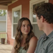A close-up, candid photograph of an authentic couple sharing a quiet, sun-drenched moment on a wooden porch of a North American / US home. The composition is intimate and cinematic, featuring warm terracotta accents in the background. The lighting is soft and natural, highlighting genuine emotion and connection.