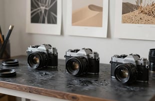 A photographer's workspace in a North American / US studio, vintage cameras, charcoal desk, and soft sand colored prints on the wall.