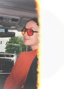Woman wearing orange aviator sunglasses in a car with a vintage film light leak effect.