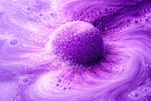 Extra large purple bath bomb fizzing in water with thick foam and cloud-like bubbles.