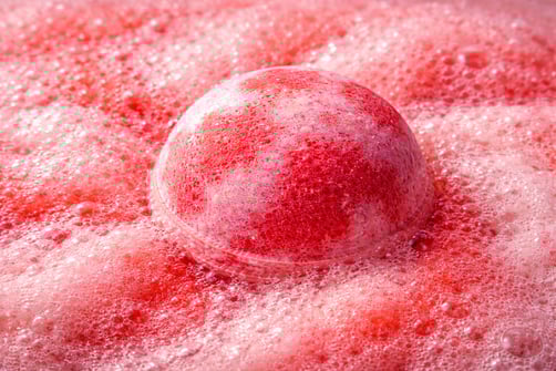 Oversized red and pink bath bomb creating bold foam and intense fizz in water.