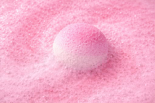 Large pink bath bomb surrounded by fluffy foam and gentle fizz.