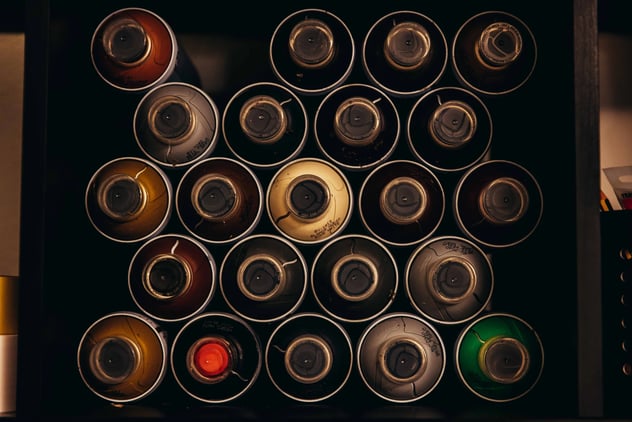 Top-down view of organized colorful spray paint cans in a storage box for graffiti art projects.