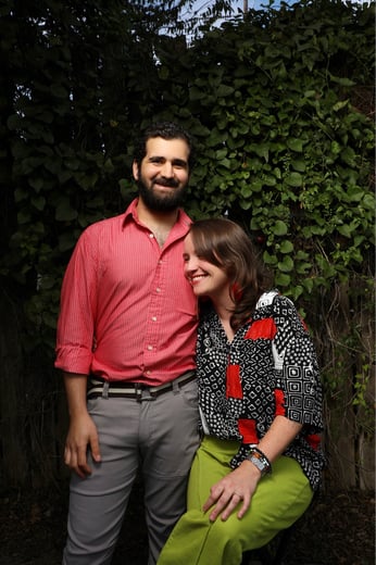 Smiling couple posing outdoors in front of a lush green ivy garden wall.