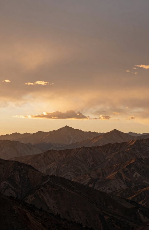 Wide cinematic sunset over a North American / US mountain range, warm earth brown and soft sand colored clouds.