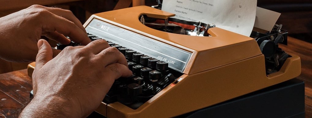 a man typing on a typewriter with a glass of wine