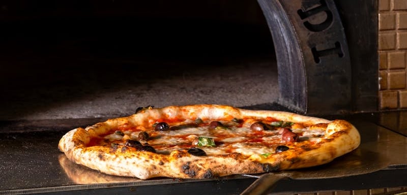 Pizza artigianale con olive appena sfornata dal forno a legna di AndrèsRosa Pizzeria ad Alseno