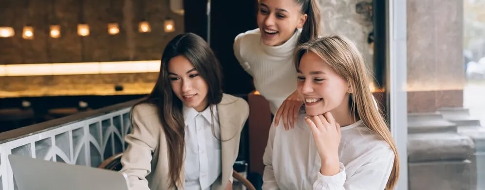 three girls sitting at a table with a laptop