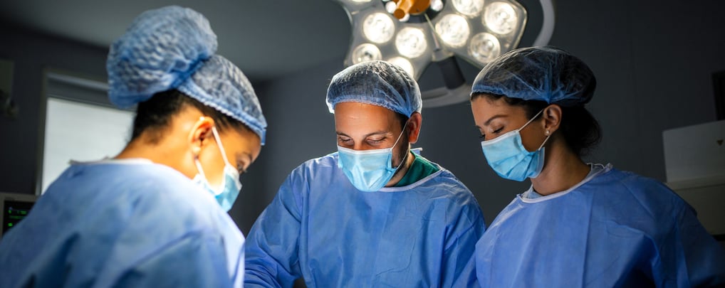 Three surgeons in blue scrubs and masks are focused on operation in operating room.