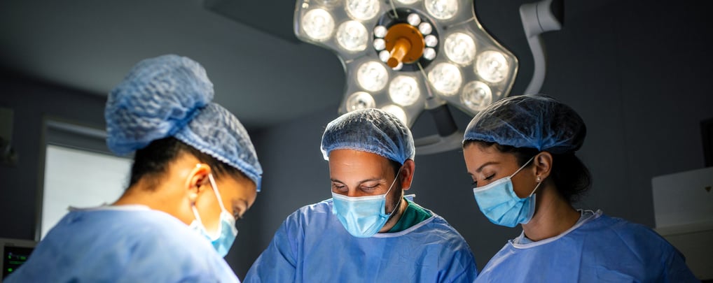 Three surgeons in blue scrubs and masks are focused on operation in operating room.