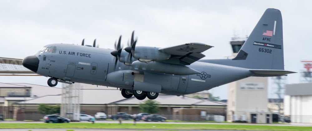 US Air Force Hurricane Hunter plane taking off with ground just below plane and control tower in back ground.