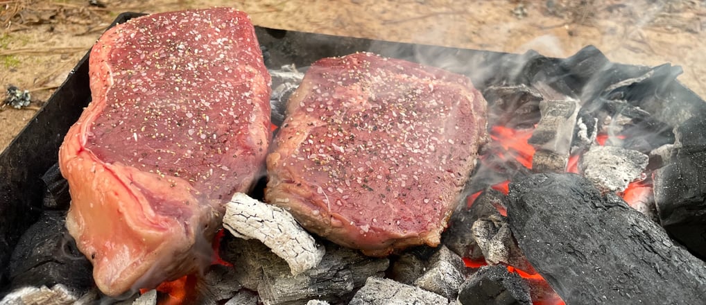 Ribeye and new york strip steaks over a live bed of lump charcoal