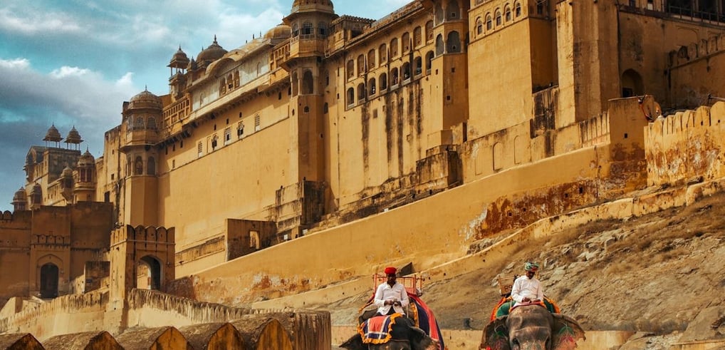 two people riding on elephants in front of a castle Amber Palace top 5 tourist places in India rajas