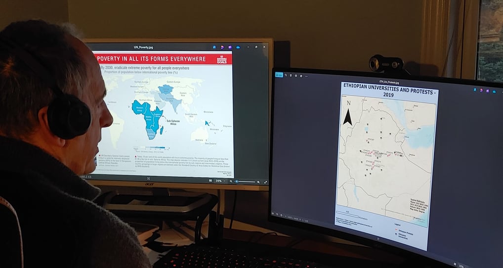 Photo of a man in front of two monitors with GEOINT maps displaying data on poverty and protests.