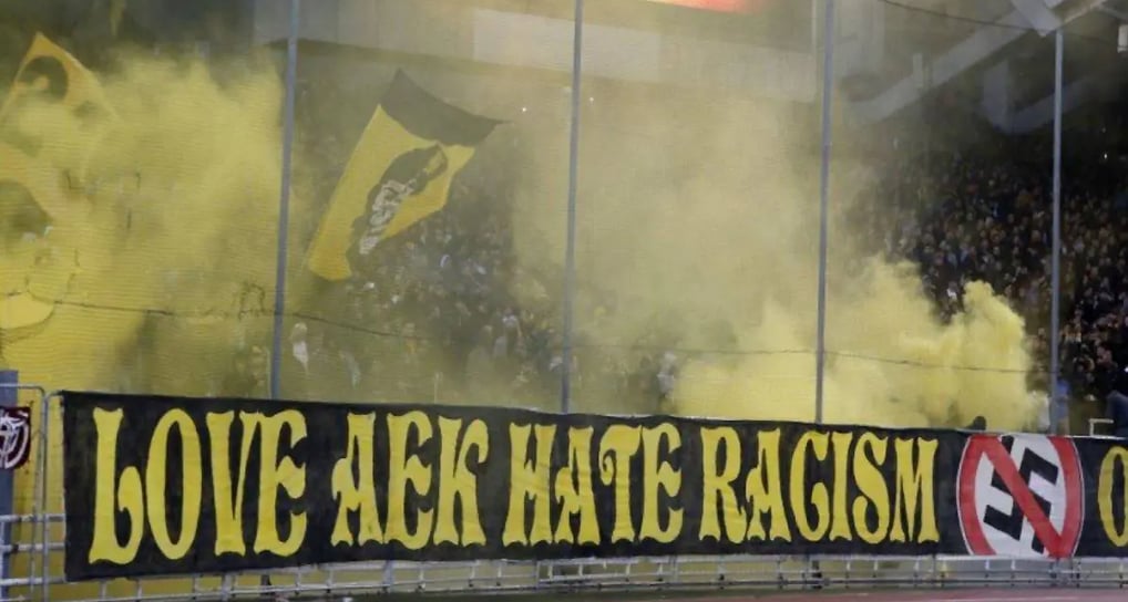 Leidenschaftliche AEK-Athen-Fans in gelb-schwarzen Farben mit Fahnen und Pyrotechnik auf den Rängen des Agia-Sofia-Stadions.