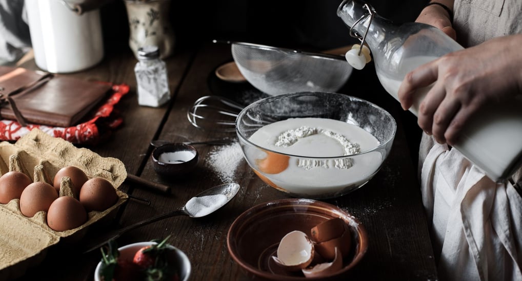 a person is pouring milk into a bowl of eggs
