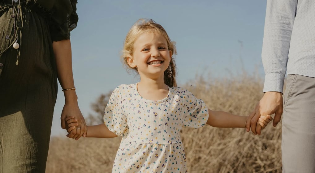 Fillette souriante en pleine nature, tenue par les mains de ses parents – photo de famille naturelle