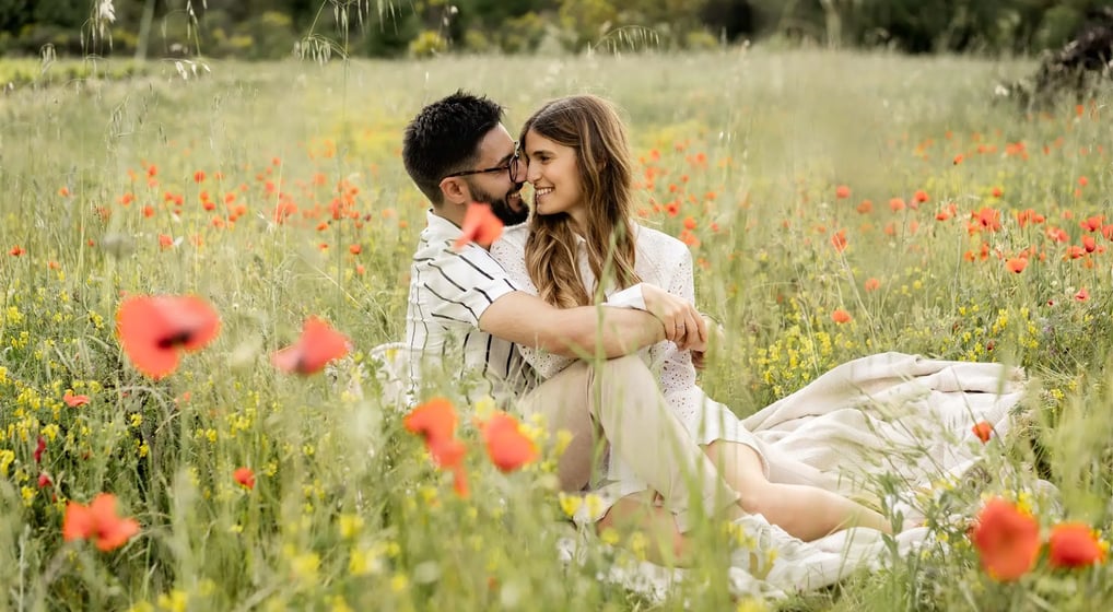 Couple sitting in a poppy field — heads together, smiling and intertwined in Provence