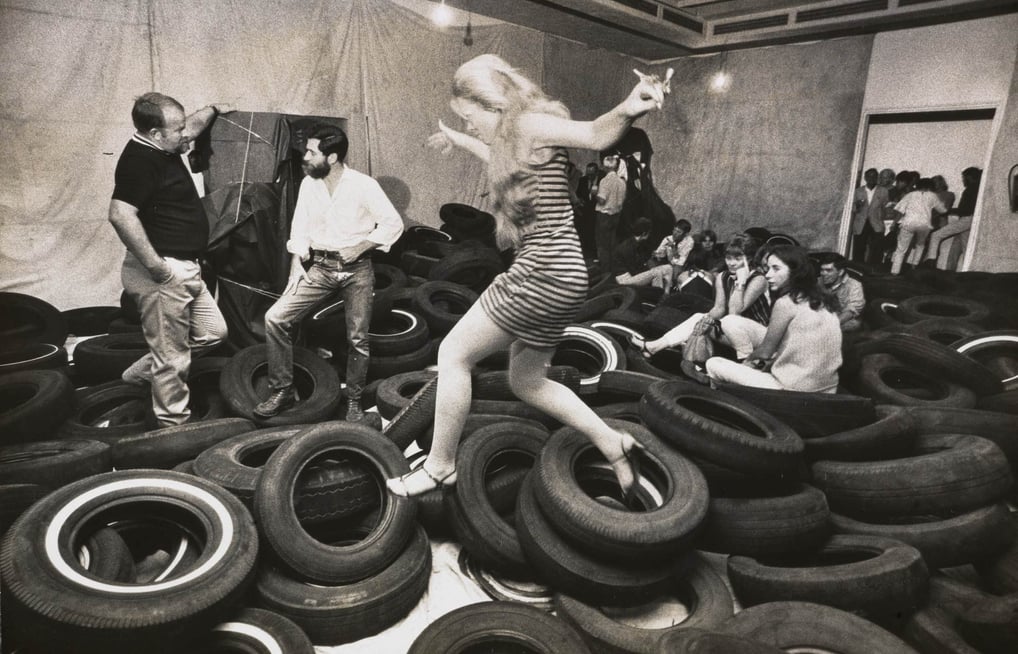 Participantes explorando pilhas de pneus pretos na instalação ‘Yard’ de Allan Kaprow, reconfigurando