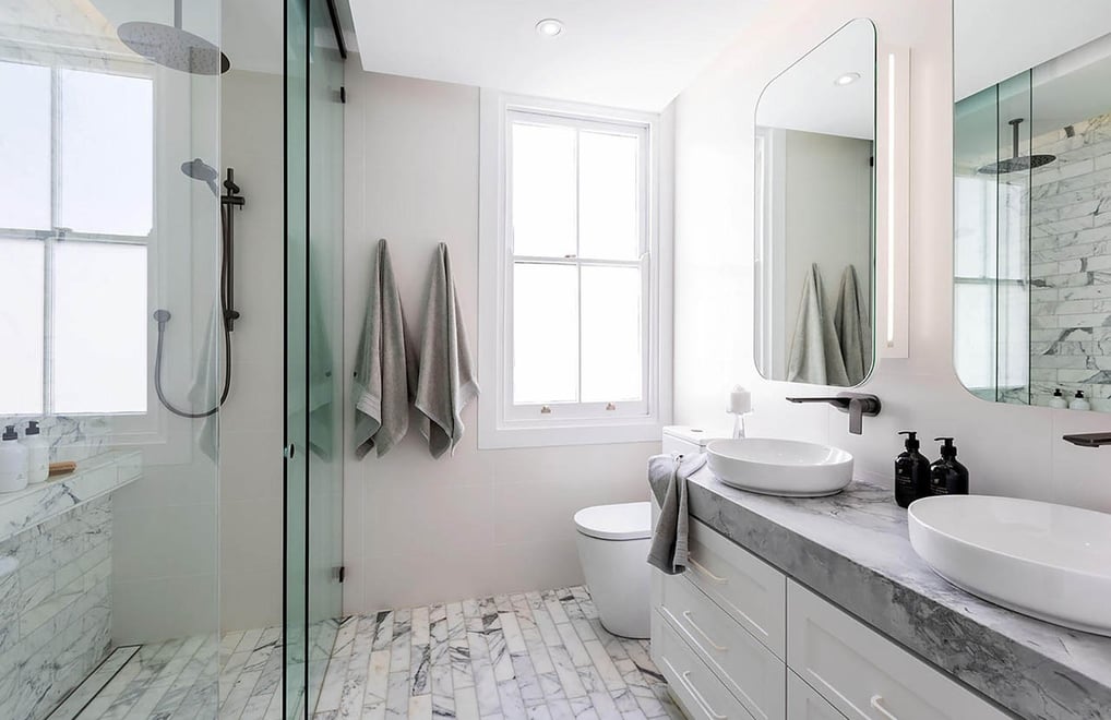 Modern en-suite bathroom featuring double vanity with two sinks, Calacatta marble tiles, glass panel