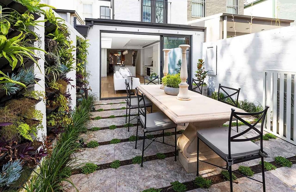 Renovated Victorian house backyard featuring lush green wall and outdoor stone dining table