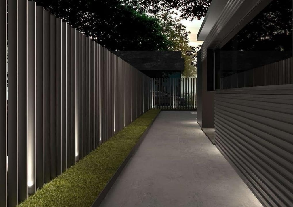 Camino peatonal flanqueado por valla metálica contemporánea con iluminación ambiental