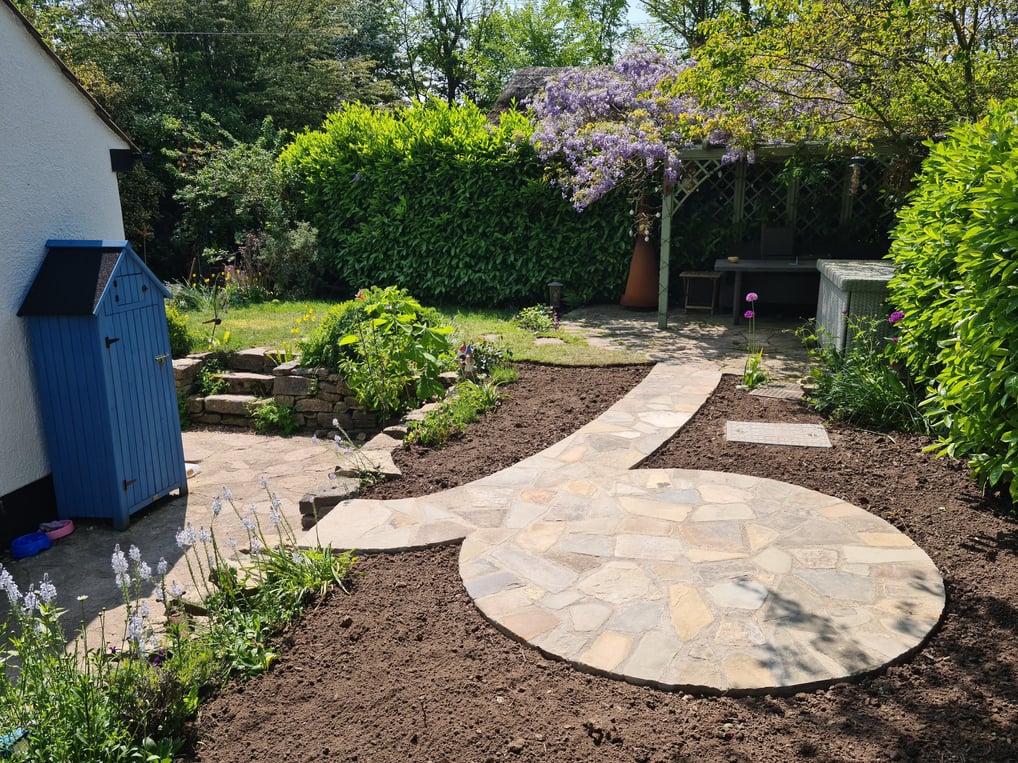 Sweeping pathway and circular patio made from old York stone in a crazy paving style.