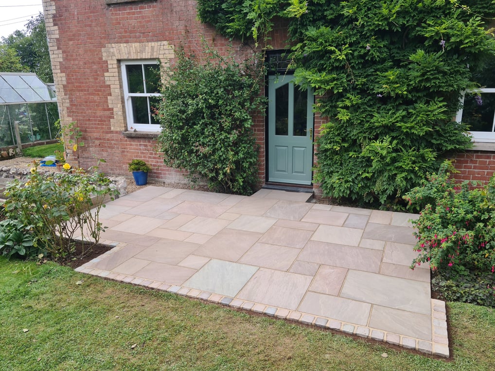 Sandstone patio laid with four different sized slabs in a random pattern, with a cobble sett edge.