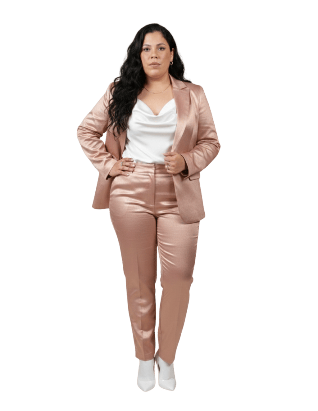 A woman posing in a shimmering rose gold satin blazer and trousers suit with a white cowl neck top.