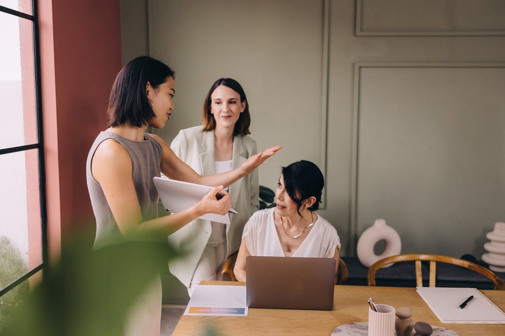 Diverse business women collaborating on a project with a laptop in a modern office.