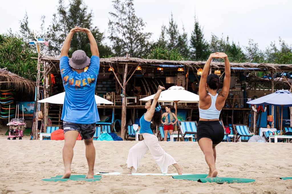 A small group practices yoga and stretching on a sandy beach at a tropical resort.